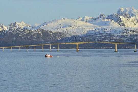 Red boat in front of Hadsel Bridge across the strait, at the back the snow-capped mountains of Hinn&oslash;ya island, Lang&oslash;ysund, near Stokmarknes, Nordland, Vesteralen, Norway, Europe