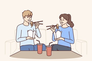 Couple eat boxed wok noodles sitting on couch using chopsticks delivered from chinese restaurant. Man and woman are eating asian fast food and enjoying taste of wok bought in takeaway cafe