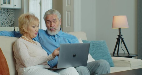 Old middle aged couple using laptop talking together doing online shopping, senior mature retired family reading discussing internet computer news. Coronavirus quarantine lockdown. - Powered by Adobe