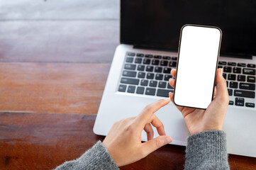 A top view of a woman pointing at a smartphone screen in her hand, using her smartphone at her desk.