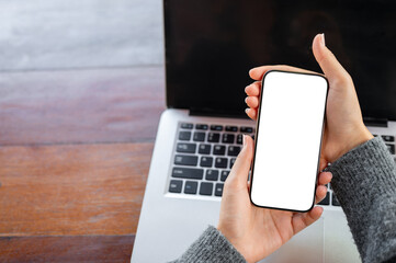 A top view of a woman pointing at a smartphone screen in her hand, using her smartphone at her desk