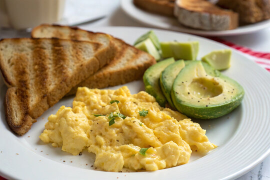 A plate of scrambled eggs with toast and avocado slices