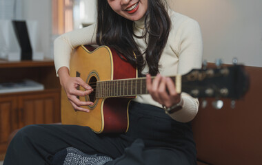 Obraz premium Woman sits comfortably on a couch, strumming an acoustic guitar with a smile. The cozy indoor setting enhances the warm, creative atmosphere, highlighting her passion for music