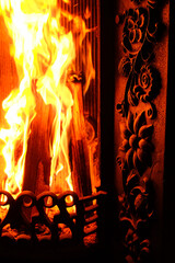 A fragment of a cast-iron fireplace insert against the background of a blazing fire. 