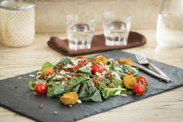 Salad with falafel, lentils and baked tomato served on stone plate