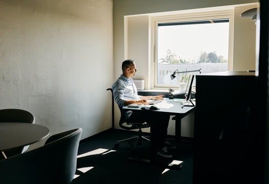 Modern Office Workspace With Professional Working at Desk by Window
