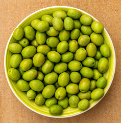Beautiful kitchen plate with fresh green matured olives on monochrome yellow orange background. Olive dish closeup, foor and drink concept