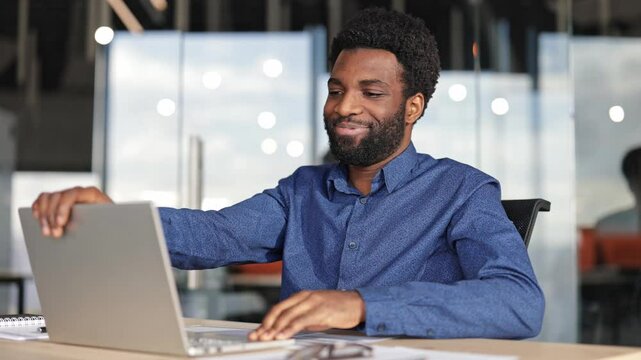 Successful young businessman finishes work on laptop, closes it, and leans back in office chair to relax.