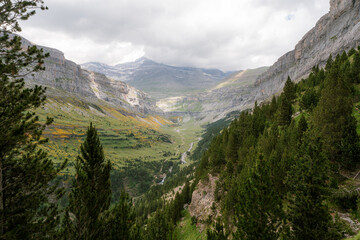 A stunning view of a green valley surrounded by towering mountains in Ordesa y Monte Perdido National Park, Spain. A perfect destination for trekking, hiking, mountaineering, and summer outdoor 