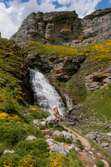 A woman hiker sits on a rock, admiring the Cola de Caballo waterfall in Ordesa y Monte Perdido National Park, Spain. A perfect location for trekking, hiking, mountaineering, and summer outdoors
