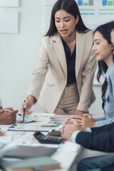 Business Meeting: A confident and focused businesswoman leads a meeting, pointing at a document and engaging in a lively discussion with her team. The image conveys professionalism, collaboration.