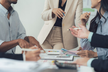 Collaborative Business Meeting: A diverse group of professionals engages in a focused discussion around a table strewn with charts and reports.