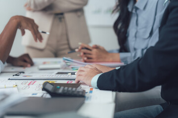 Strategic Business Meeting: A diverse team of professionals engages in a collaborative discussion around a table, reviewing financial documents and charts.