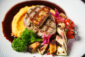 Succulent beef filet with foie gras, served with velvety mashed sweet potatoes, grilled zucchini, and cherry tomatoes. A gourmet meal in a sophisticated dining setting