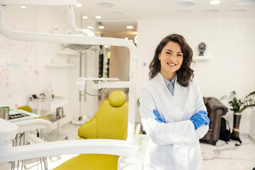 Portrait of happy dentist standing at dentist office with arms crossed and smiling at the camera.