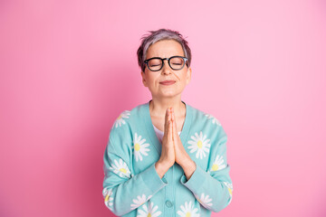 Elderly woman in a daisy cardigan expresses gratitude with eyes closed against pink. Stylish...