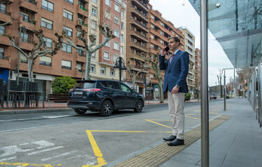 Fototapeta premium Businessman waiting at bus stop and talking on phone