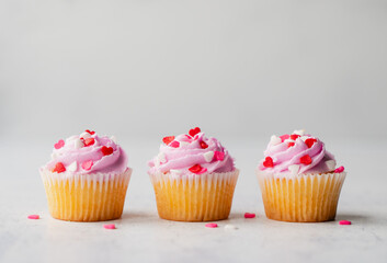 Three cupackes with pink frosting and hearts on white background.