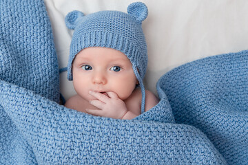 cute baby in a hat with ears and under a blanket sucking his hand