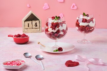 Dessert, trifle Red velvet with butter cream and raspberries in glasses on pink concrete background with Valentine's Day decor. Dessert for lovers. Portion desserts.