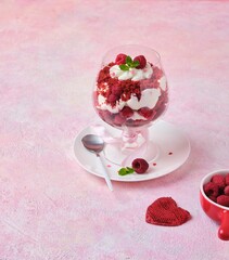 Dessert, trifle Red velvet with butter cream and raspberries in glasses on pink concrete background with Valentine's Day decor. Dessert for lovers. Portion desserts.
