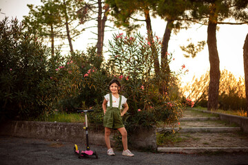 small happy girl standing in the park next to her scooter looking at camera © Victoria