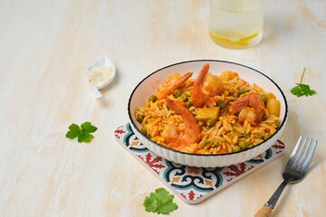 Orzo pasta with carrots, green peas and shrimps with tomato sauce in a white plate on a light concrete background. Seafood recipes.