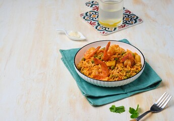Orzo pasta with carrots, green peas and shrimps with tomato sauce in a white plate on a light concrete background. Seafood recipes.