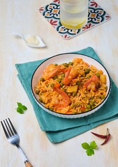 Orzo pasta with carrots, green peas and shrimps with tomato sauce in a white plate on a light concrete background. Seafood recipes.