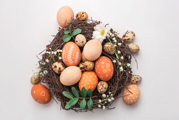 Easter nest with hand-painted eggs and quail eggs on a light background. A rustic spring composition with natural elements, fresh greenery and floral details.