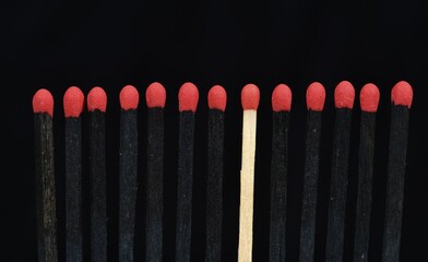 A bright match among several black matches, black background, symbolic image, exclusion,...