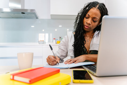 Young woman writing in a notebook and using a laptop while working remotely from home