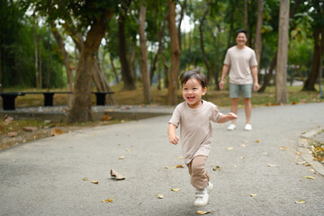 Joyful young child running along a park pathway with his father