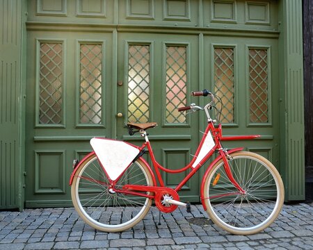 Red bicycle with empty signboard in front of a green gate in Ystad, Scania, Sweden, Europe