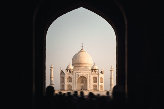 Taj Mahal Bei Sonnenaufgang in weichem, rosanen Licht umrahmt vom Eingangs Bogen durch die Besucher Menschenmassen str&ouml;hmen