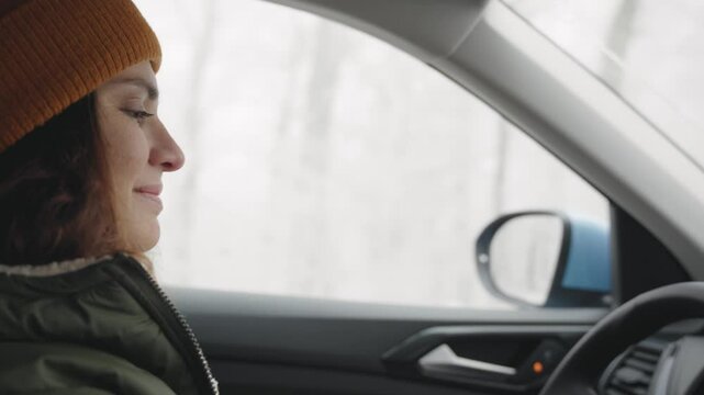 Portrait of a young cheerful woman in winter clothes driving a car on a winter road