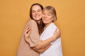 Two women stand close together with bright smiles, enjoying a moment of affection and happiness against a vibrant yellow background. Their bond reflects warmth and love