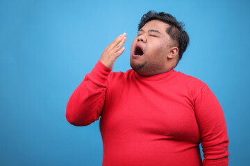 Fototapeta premium Young Fat Man Feeling Bored And Yawning Over Blue Background 