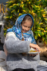 A beautiful Russian girl in a fur coat and a headscarf is sitting on the porch of a wooden house. Family values, traditions and home comfort.Maslenitsa holiday, winter send-off and spring meeting