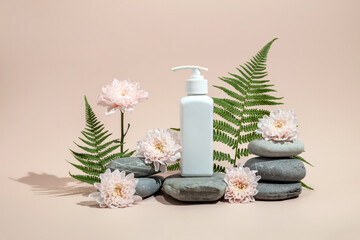 bottle for cosmetics on a stone podium surrounded by fern leaves and chrysanthemum flowers. A mock-up of organic cosmetics on a light background.