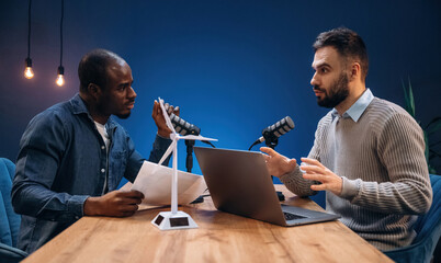 Side view, talking. Two radio presenters recording an audio broadcast in a studio