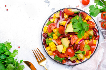 Mexican vegan corn salad with red beans, avocado, tomatoes, onion and cilantro. White background, top view