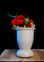  A bouquet of vibrant red roses and delicate white blossoms arranged in a simple ceramic vase against a black background, highlighting contrast and elegance.