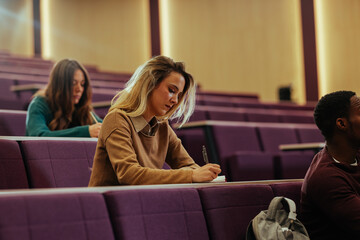University students taking notes during lecture in auditorium