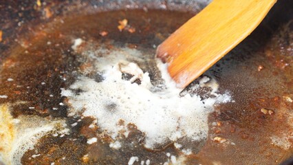 A pot with hot oil and cleaning powder being stirred with a wooden spoon.