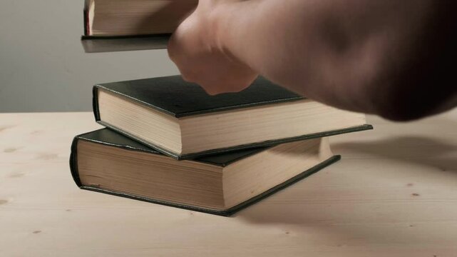 Hand replacing one book from a stack of three hardcover books. They are hardcover green books. 50fps