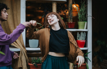 Obraz premium A young couple shares a joyful moment, dancing playfully in a cozy setting surrounded by plants. The image captures a sense of carefree happiness and connection.