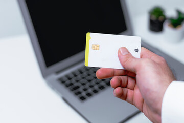 Close-up of male hand holding credit card in front of laptop