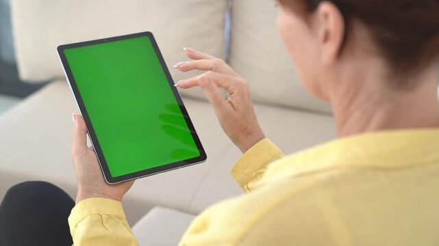 Tablet with green screen held by woman indoors, showcasing touchscreen gesture, modern technology, cozy home interior, concept of digital interaction and customizable media display