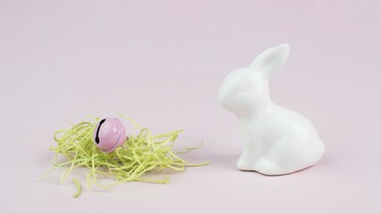 Easter bunny or rabbit, nest with green grass and a bell, spring holiday greeting card, pink pastel color, minimailism
